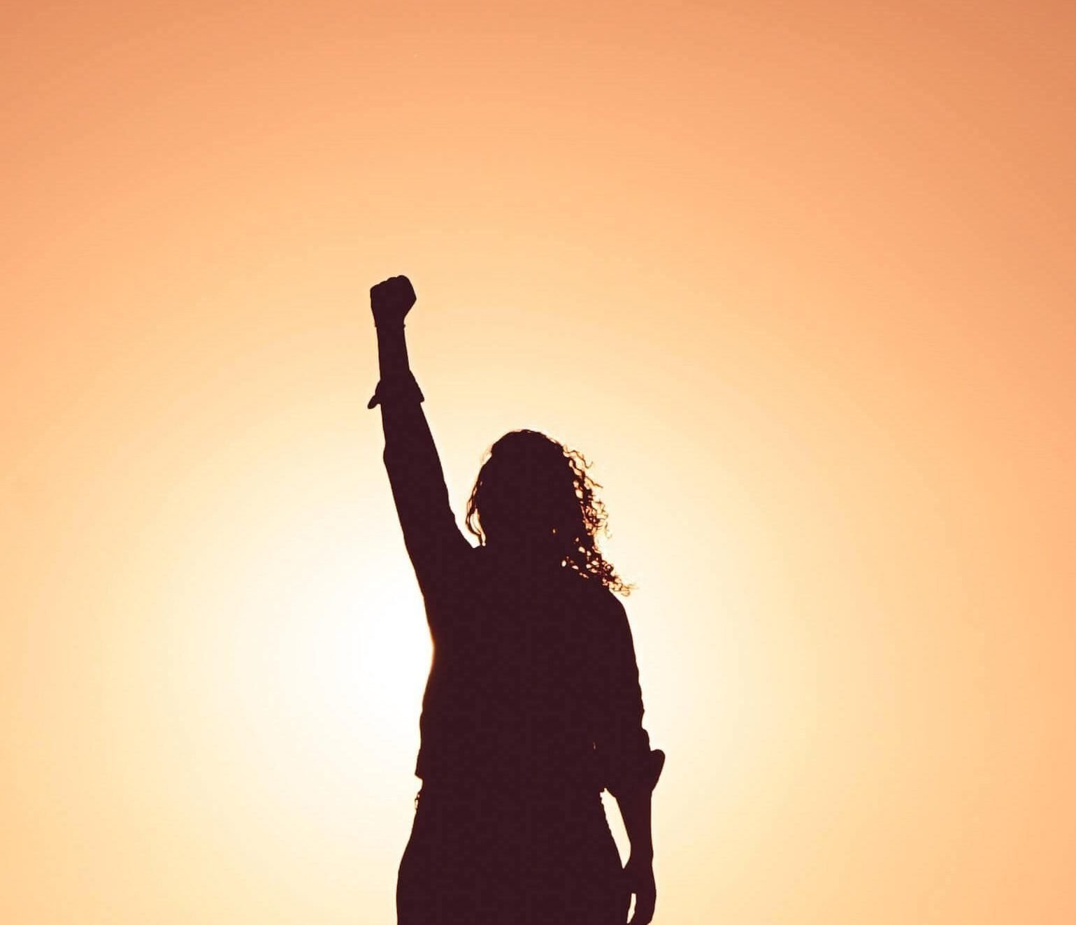 silhouette of woman putting fist in the air at sunset as she overcomes the thought of "I don't know what to do with my life"